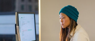 A close-up of a person wearing a beanie and looking at a computer screen.