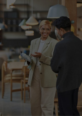 A woman talking to a man in a room with a chair and a white lamp shade.