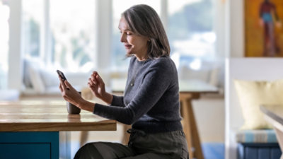 A woman in a grey sweater sitting at a table looking at her phone.