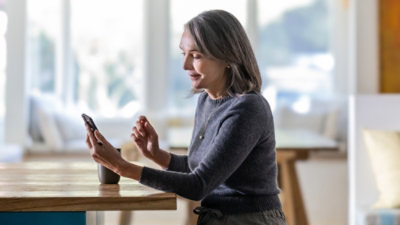 A woman in a grey sweater sitting at a table looking at her phone.