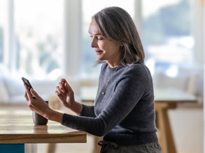 A woman in a grey sweater sitting at a table looking at her phone.