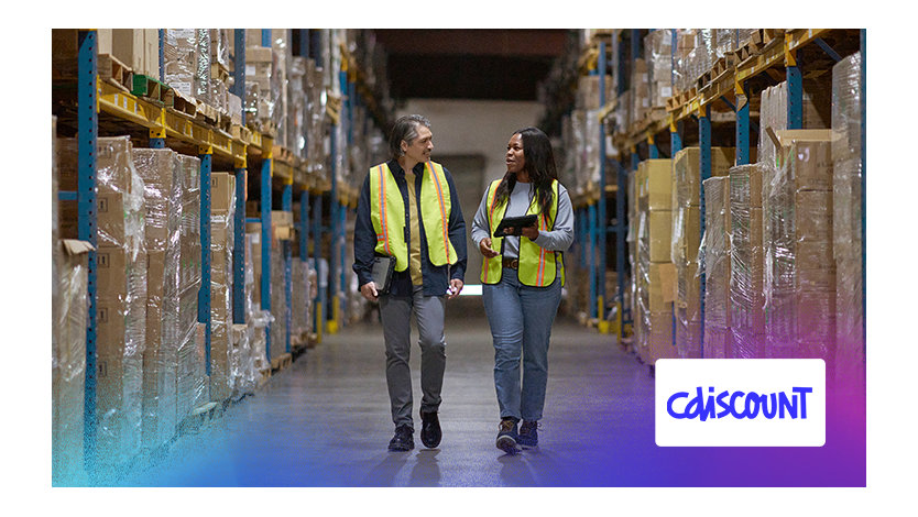 Deux personnes en gilets de sécurité marchent dans un entrepôt, observant leur environnement de travail.