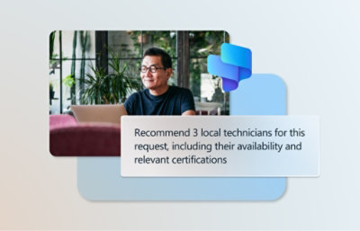 A man wearing glasses and smiling while sitting at a desk with a sign in the background.