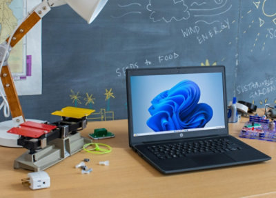 A laptop on a desk with a chalkboard in the background displaying the words WIND, FOOD, ENERGY, and SUSTAINPELE.