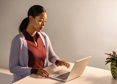 A woman standing near a table using a laptop.