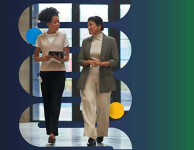 A woman in a white sweater and black pants holding a tablet walks in a hallway with a person in a suit.