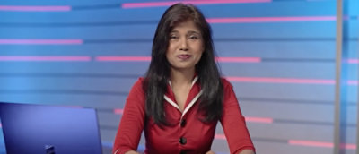 A woman wearing a red shirt stands under a blue sky with clouds.