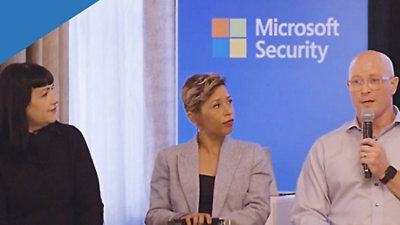 A group of people standing near a blue sign with the text Microsoft Security.