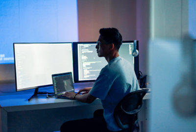 机に向かってノート PC を使っている男性。