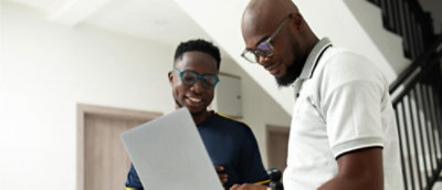 Two employees in a modern office smile as they discuss something displayed on the computer screen between them.