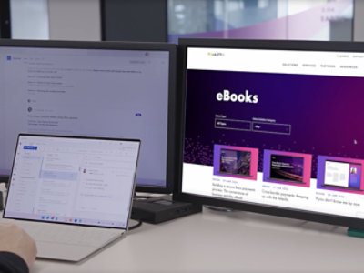 A laptop and two monitors are set up on a table, with text on one screen that reads eBooks.