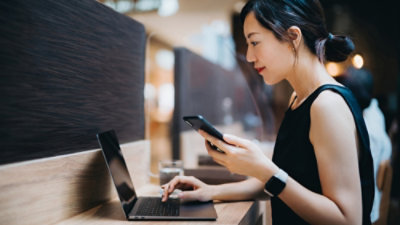 Person working on a laptop at a shared workspace desk while checking information on a smartphone