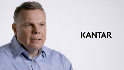 A close-up of a man wearing a blue shirt with the text KANTAR visible.