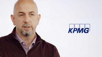 A man with a goatee wearing a purple shirt with the text KPMG visible.