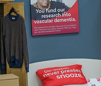 Retail display with a printed sign about vascular dementia research and a red cushion reading “Our research never presses snooze."