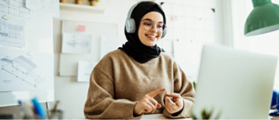 A woman wearing headphones and a headset pointing at a computer screen.