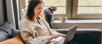 A woman working on her laptop with a cat strolling near a window