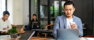 A man holding a cup and looking at a laptop.