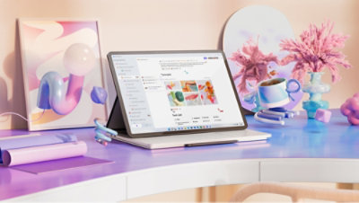 A laptop on a desk with a cup of coffee and pink flowers nearby.