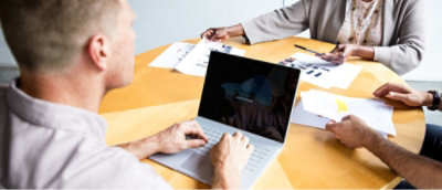 Three individuals engaged in a business meeting with documents and a laptop on a table.