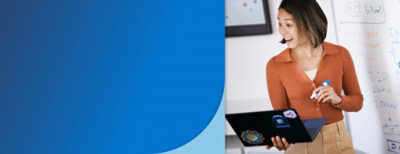 ノート PCとマーカーを持ち、メモが書かれたホワイトボードの前に立つ人。