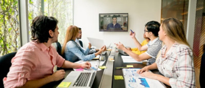 Diverse team in a meeting discussing with a colleague on a video call, laptops and documents on table.