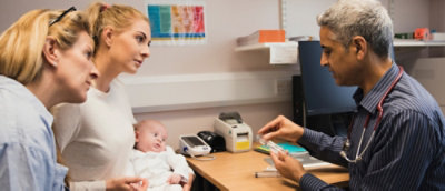 Doktor objašnjava lekove dvema ženama koje drže bebu u kliničkoj ordinaciji.