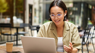A person wearing glasses and earbuds sits at a table using a laptop.