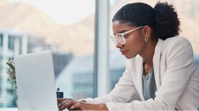 A woman in a white suit and glasses working on a computer.