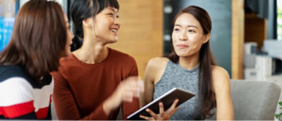 A woman wearing a red shirt is holding a book while looking at another woman.