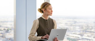 A person holding a laptop while looking out a window.