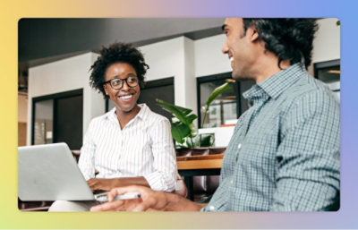 A man and woman sitting at a table looking at a laptop.