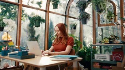 Une femme assise à un bureau écrivant avec un stylet sur une tablette, à côté d’un clavier.
