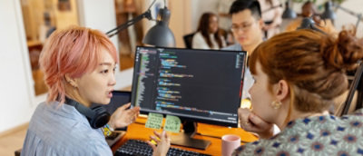 A man sitting at a desk with a computer screen in front of him and a whiteboard nearby.