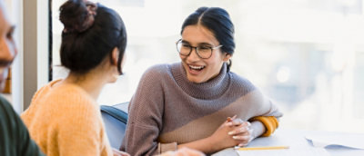 A woman laughing while another woman is sitting.