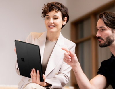 A woman and a man are sitting down and pointing at a laptop, engaging in a discussion.