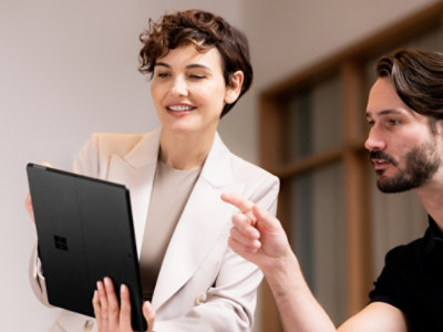 A woman and a man are sitting down and pointing at a laptop, engaging in a discussion.