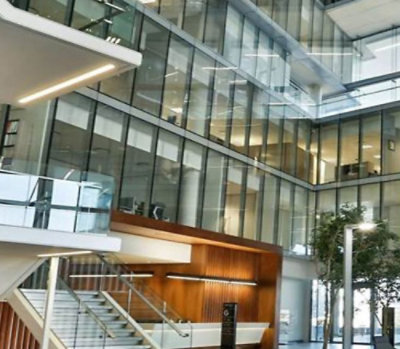 A building with glass walls, visible stairs, metal railings, trees, and a light pole.