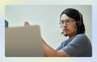 A person wearing headphones and glasses is gesturing while looking at a computer screen