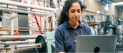 A woman sitting in the factory and working on the laptop