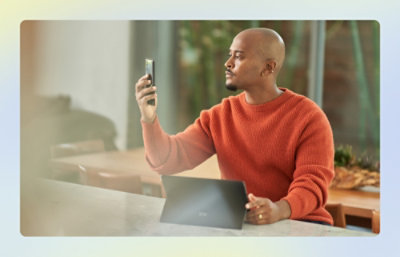 Person sitting at desk holding and looking at smartphone, Surface Tablet sits in front of them
