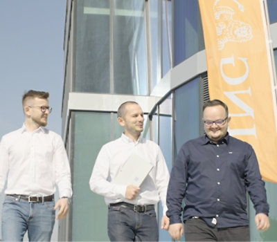 Three people walking outside a modern glass building with an orange banner