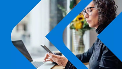 Person using smartphone and laptop at a desk near a window