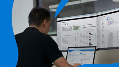 Individual working on laptop with two large monitors displaying dashboards