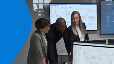 Three people collaborating in front of a large screen with analytics dashboard