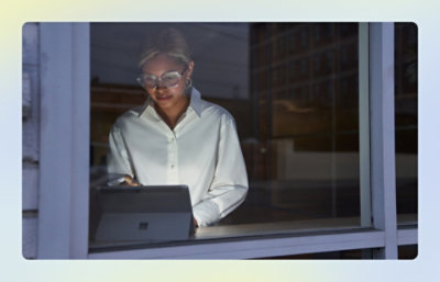 Person using a tablet while standing by a window at dusk.