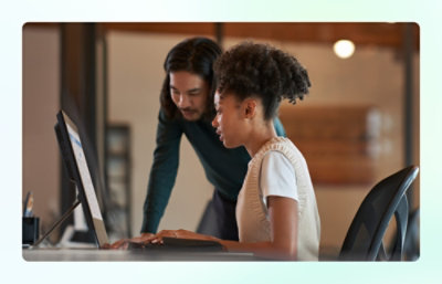Person working at a desktop computer with guidance from a colleague