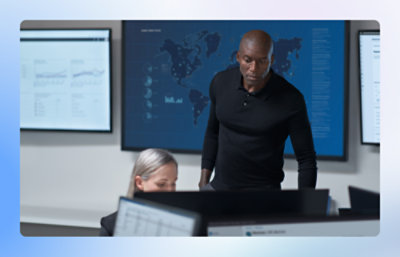 Two people working in a control room with large data screens.