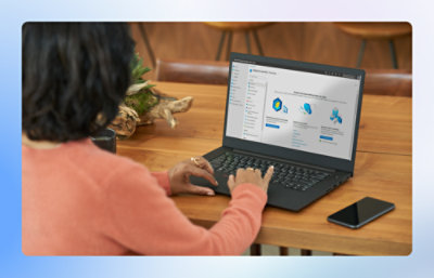 Person using a laptop at a wooden table with a phone beside them.