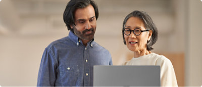 Un bărbat cu barbă și o femeie cu ochelari privind un laptop.